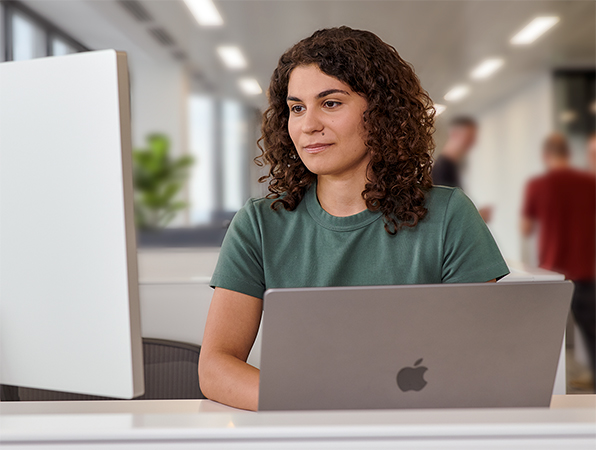 Ein Apple Teammitglied arbeitet in einem Büro an einem MacBook und Studio Display.