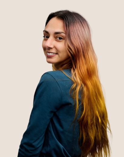 Portrait of a smiling Apple Retail team member with long brown hair looking over her shoulder at the camera.