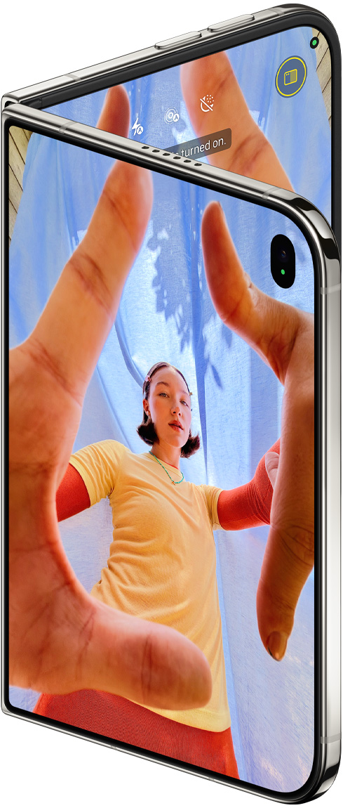 iPhone Duo, color blanco estrella, semiabierto, app Cámara en la pantalla exterior con la cámara frontal Center Stage, la pantalla interior muestra la fototeca