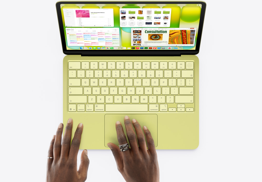 MacBook Neo, couleur jaune agrume, une main sur le trackpad, plusieurs fenêtres ouvertes, dont les apps Musique, Calendrier et Microsoft PowerPoint