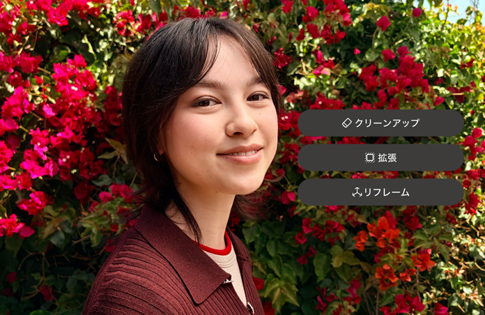 茶髪の人物が微笑んでいる写真。茶色のセーターを着て、赤い花に囲まれている。写真上に表示されている「クリーンアップ」「拡張」「リフレーム」のオプションを使ったAIによる写真編集を示している