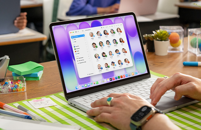 A teacher sits with an open Mac, and the Classroom app shows a full student list on screen