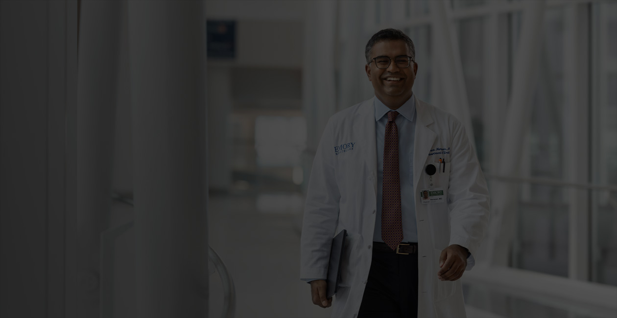 En lege holder en MacBook under høyre arm mens han går.