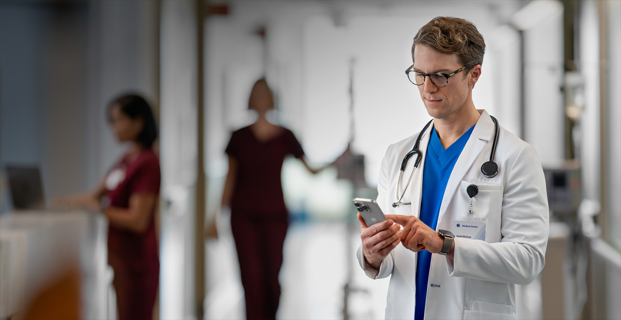 En mannlig helsearbeider ser på en iPhone inne på et sykehus.